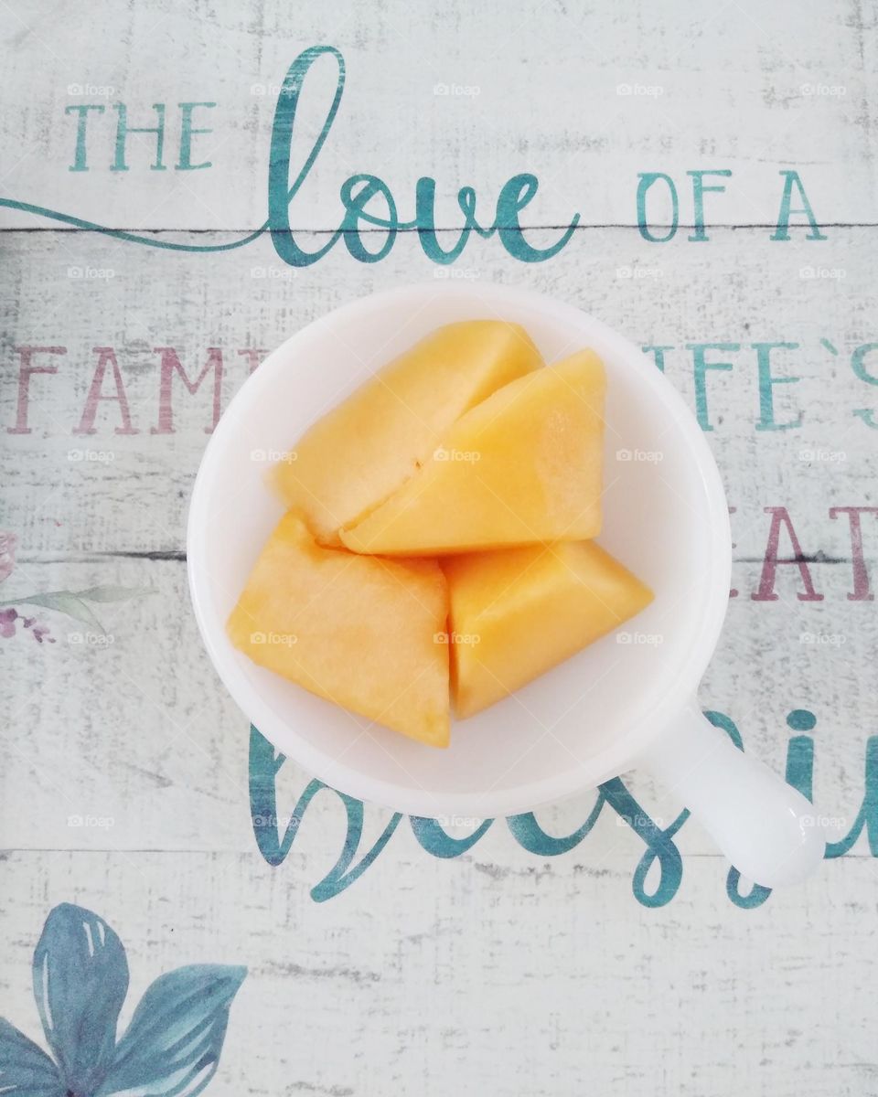 Chunks of cantaloupe in a saucer on a placemat that says " The love of a family is life's greatest blessing"