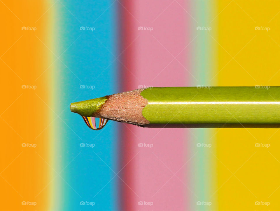 Colorful reflection in a water drop on the top of a green pencil, colorful background