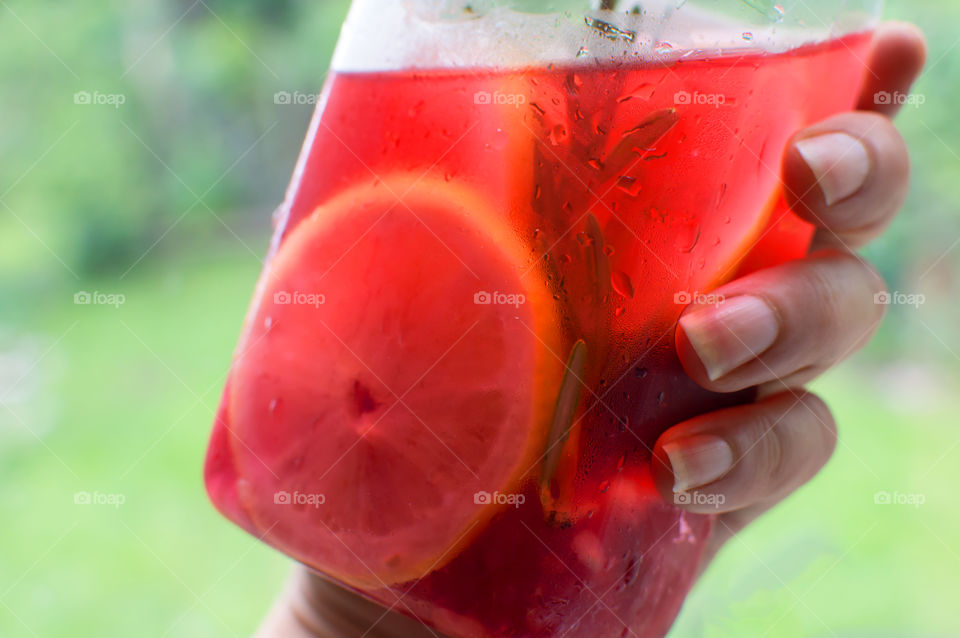 Woman's hand holding a cold bottle of aromatic and antioxidant homemade flavored water made from raspberry, lemon slice, fresh rosemary and blueberry extracted juices on hot summer day 