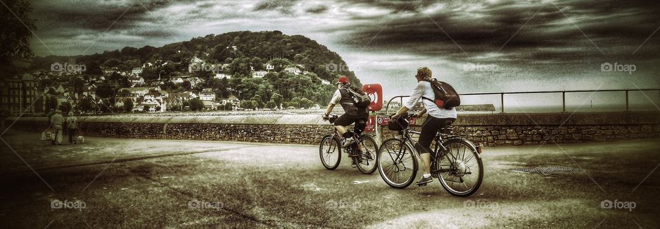 Cycling. Two cyclists cycling along the seafront of an English resort town on the promenade 