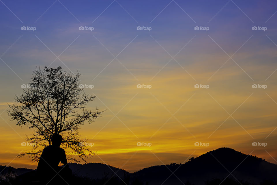 The morning sun light behind the mountains with the shadow of a man and the tree.