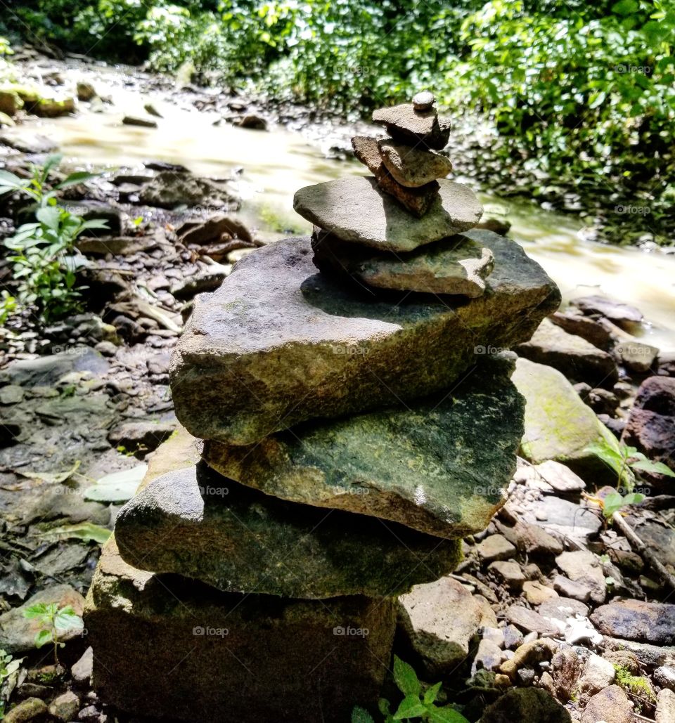Pile of stones left by hikers along a creek in a park on a sunny summer day