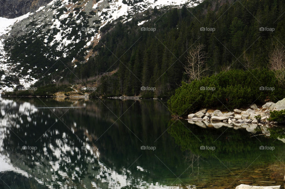 Snowy mountain and trees reflecting on lake in poland