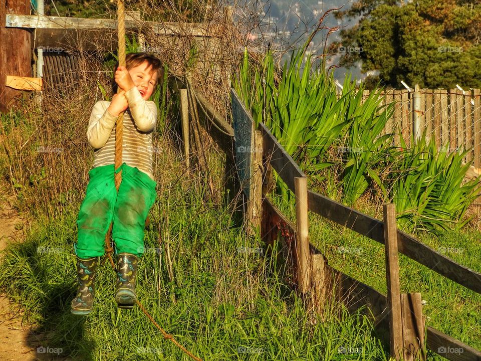 Happy Boy Riding A Zipline. Young Boy Swinging Down A Zipline And Having Too Much Fun
