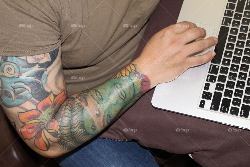 Man with tattooed arm working on his laptop 