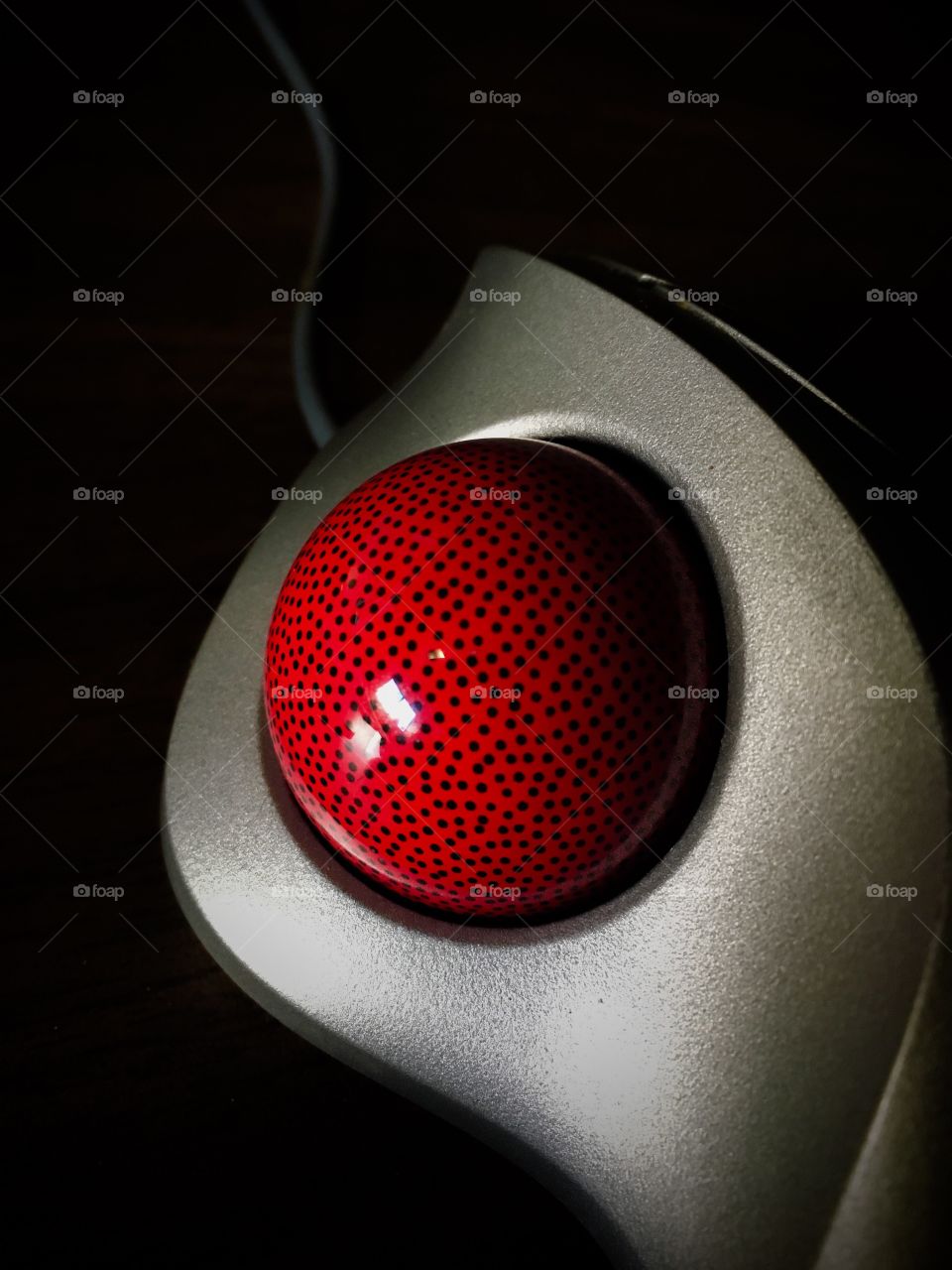 Silver thumb-controlled trackball mouse with a red ball with black specks on a black background