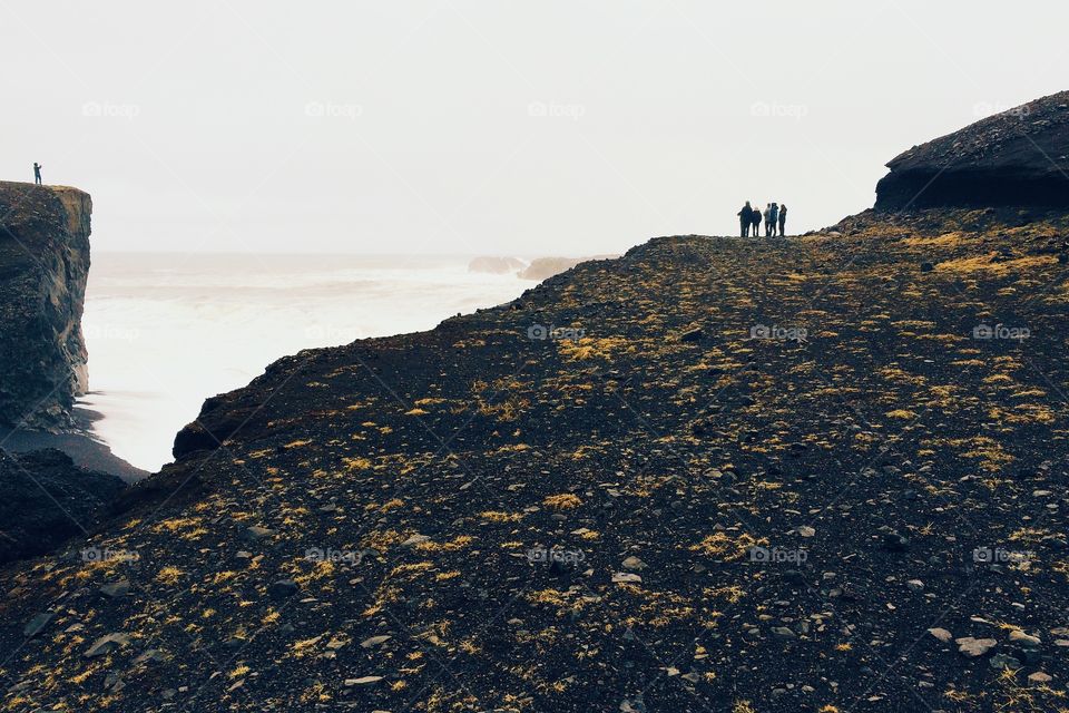 People standing at the edge of a cliff, overlooking the Atlantic Ocean. . Golden path over black sand leading to oceanic overlook in Iceland