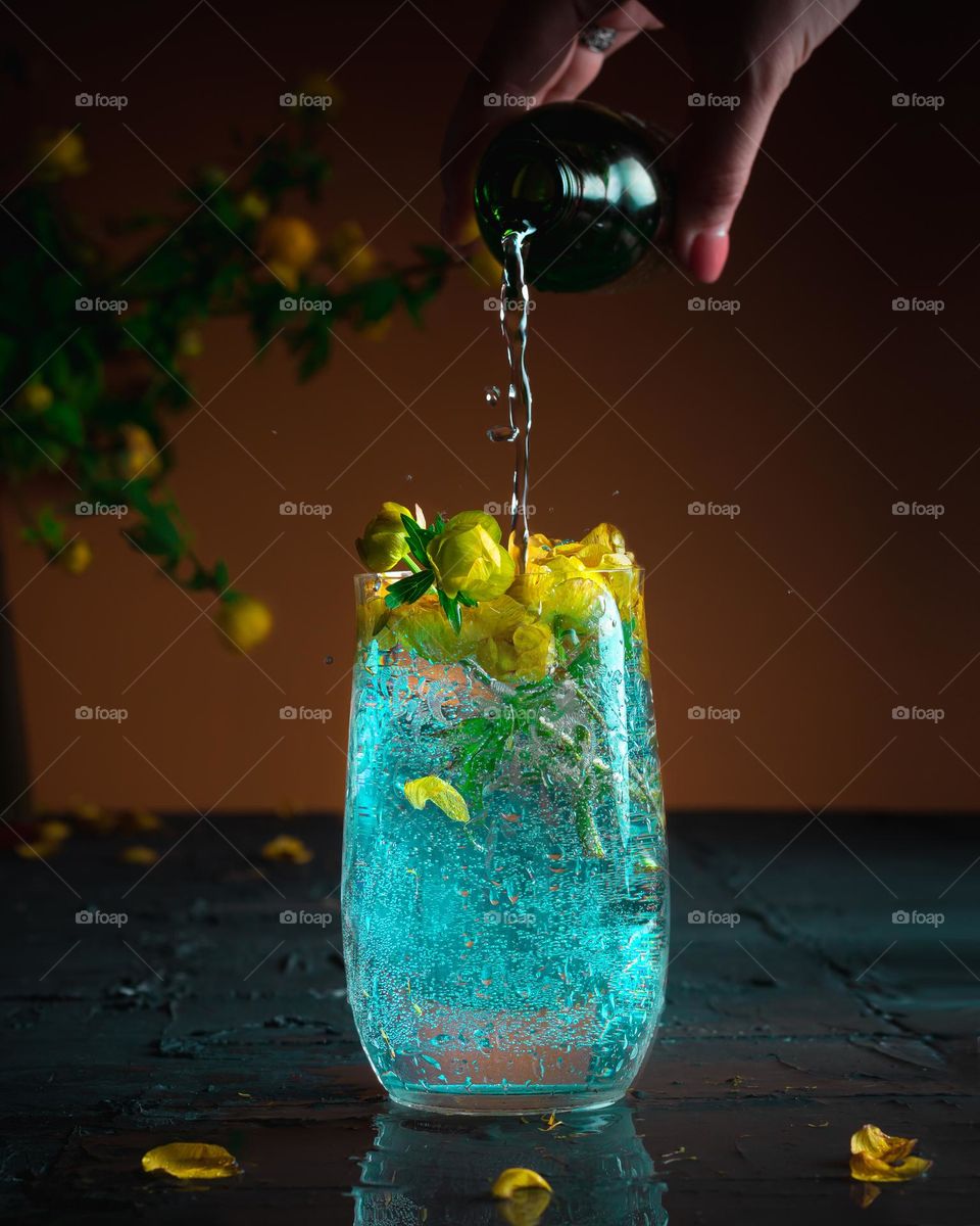 Closeup glass of blue lagoon cocktail decorated with flowers at festive bar counter background. High quality photo