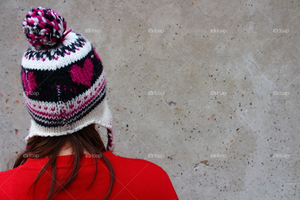 Girl with red pullover with hand on gray background with heart decorated hat