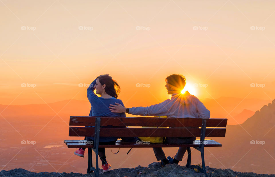 Couple flirting on a bench against sunset