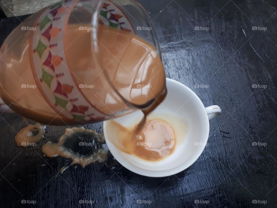 a cup of mocha coffee that was being poured but spilled over a small glass in the morning