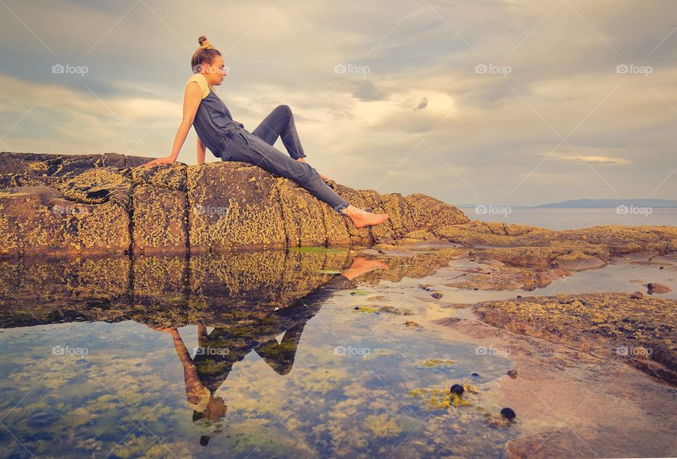 Beautiful young girls sitting on a rock reflected in water