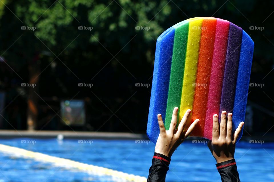 a kid holding a swimming kickboard and preparing to dive in a pool