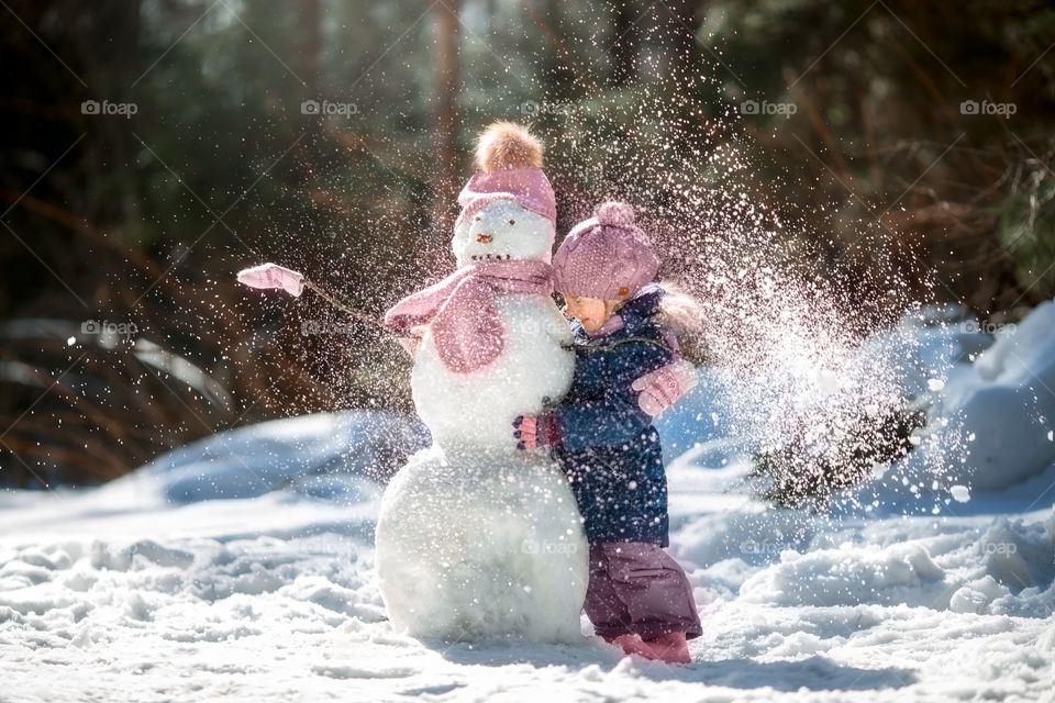 Little girl with snowman in winter forest at sunny day