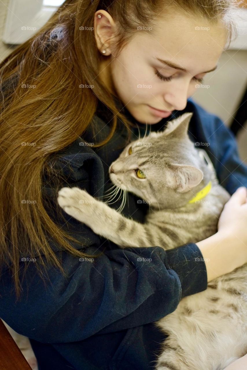 Endearing and eternal bond between a girl and cat. Tabby cat hugging young woman with long brown hair. 