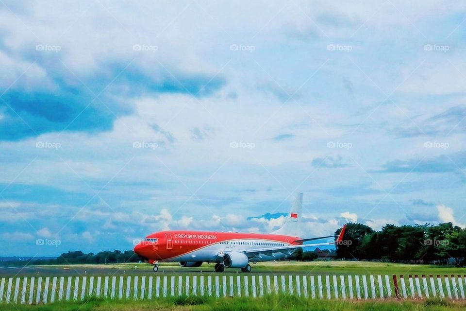 Long distance view of an airplane with red livery and the words "REPUBLIK INDONESIA" on the runway