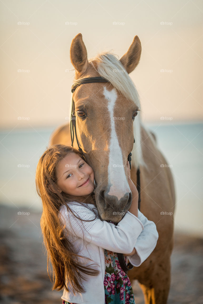 Happy girl with palomino horse at sunrise on a sea