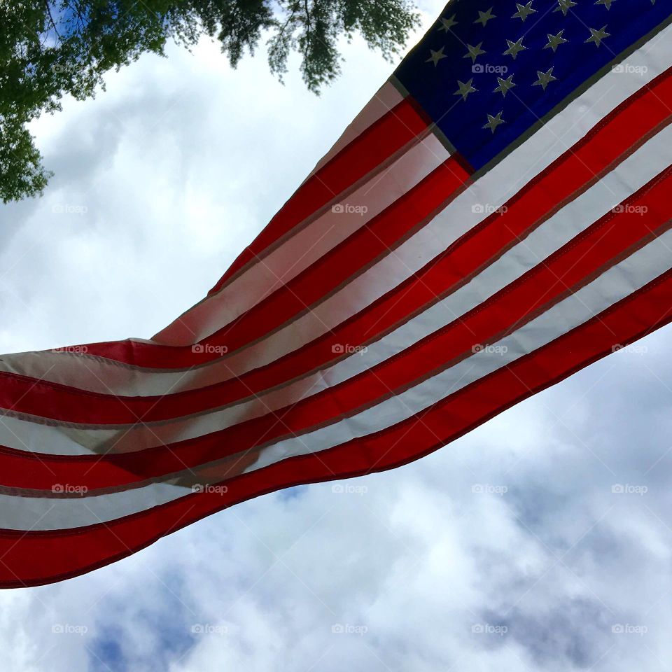 American Flag in wind, looking up, against cloudy sky and tree leaves. Stars and Stripes!