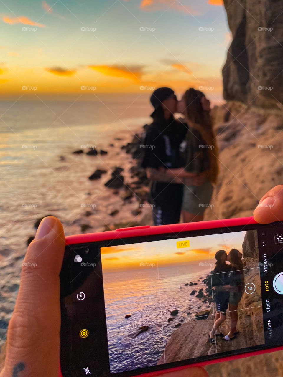 Photo to a mobile photographing a couple of girls kissing on the beach during sunset
