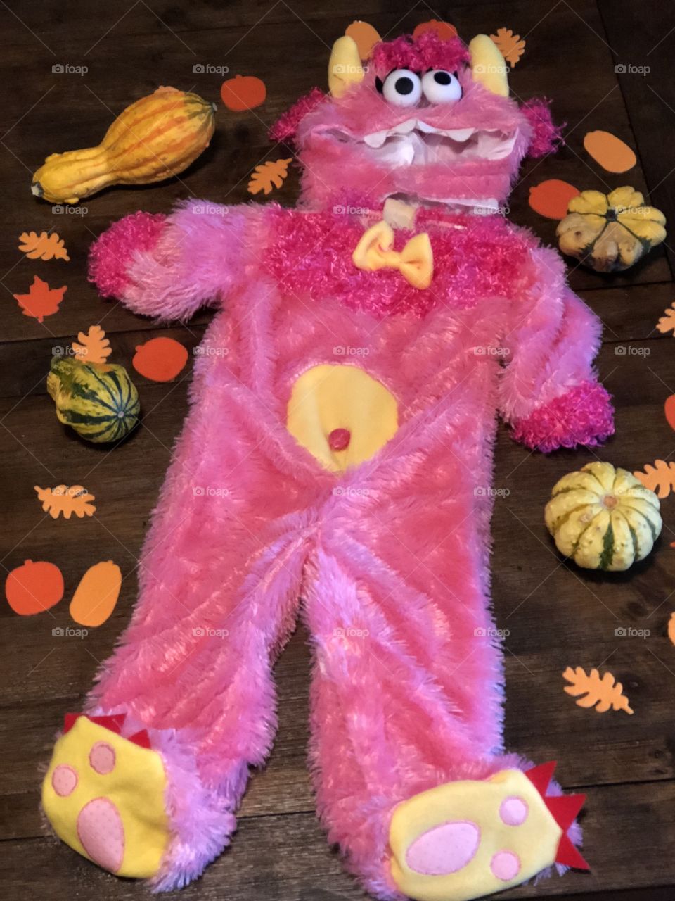 Fall themed background surrounds a toddler sized pink monster Halloween costume