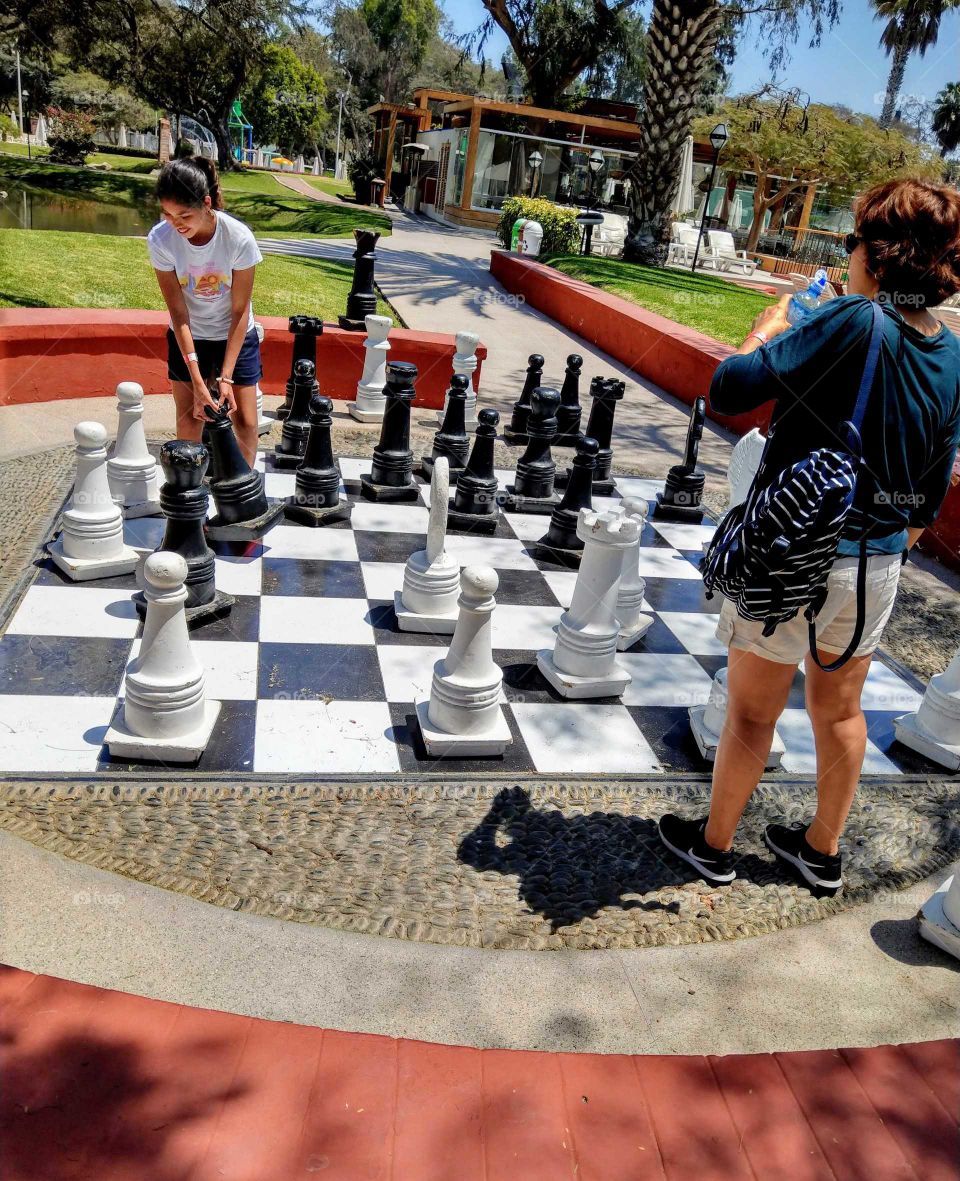 Shapes: rectangle.playing chess outdoor. two girls interested chess game.
checkerboard is square. all are big, very funny.