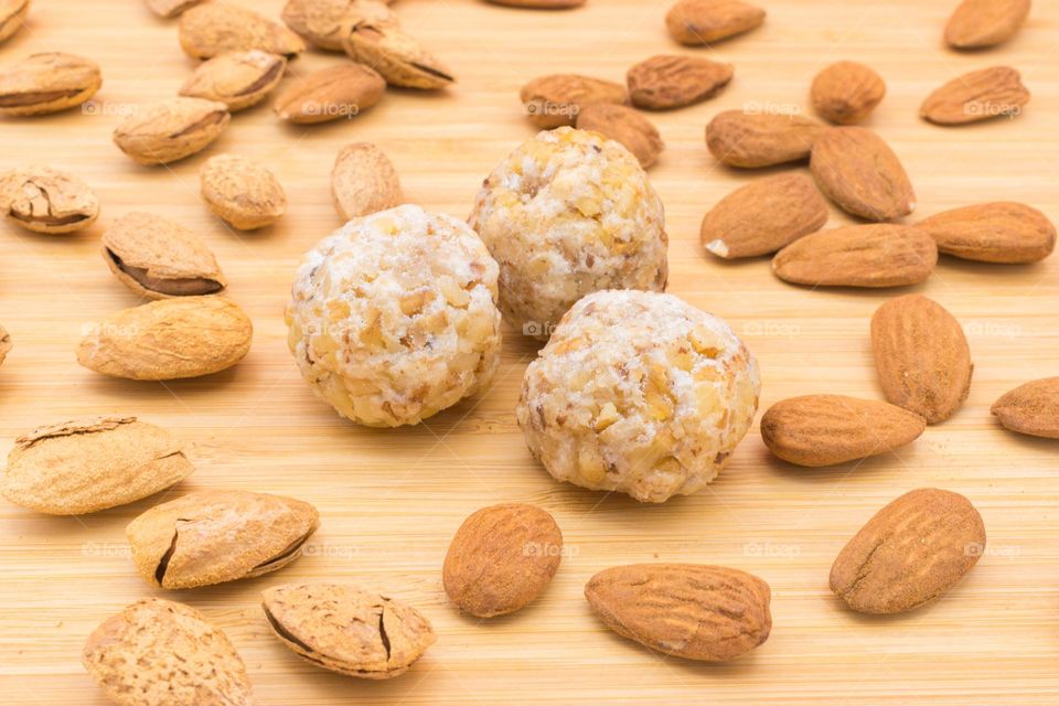 Panellets on a wooden surface, surrounded  by almonds. Panellets are traditional sweets for All Saints' Day in Catalonia, the Balearic Islands, Levante and Aragon.