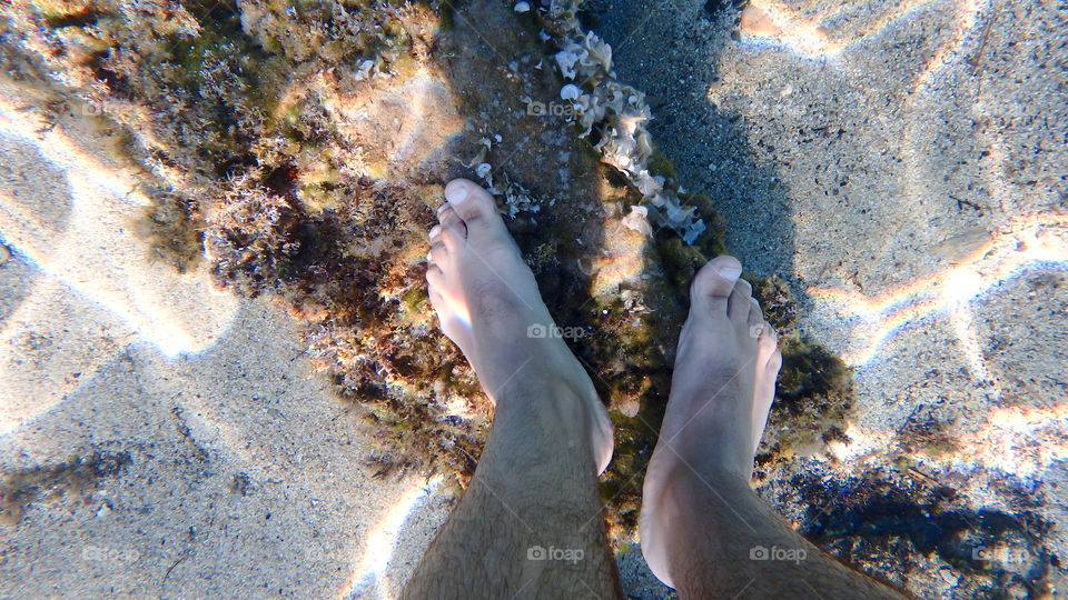 human feet underwater on rock