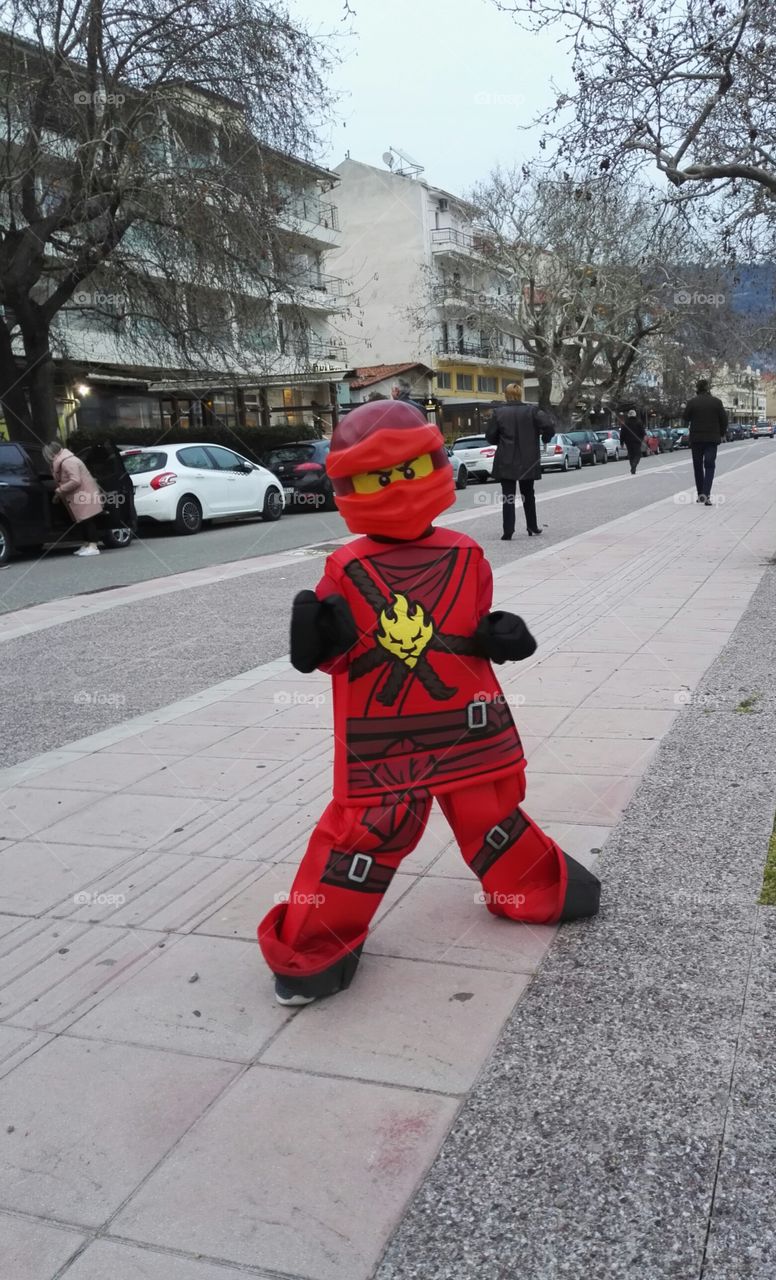 child in red lego ninja costume on street in Nafpaktos, carnival