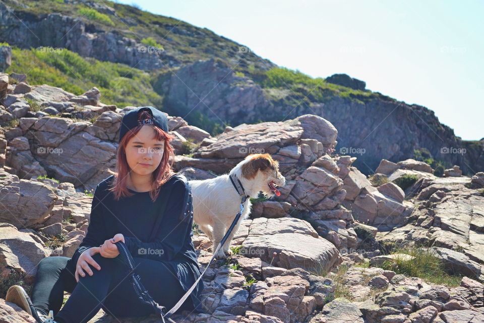 Girl sitting with a dog among a rocky landscape