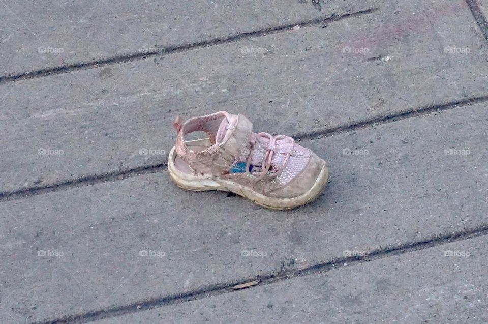 A dirty lost baby pink shoe is all alone on the street.