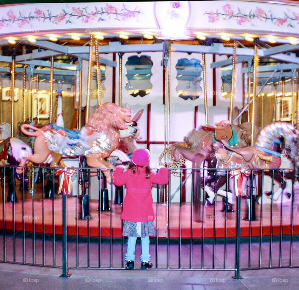 Little girl watching old-fashioned carousel going around 