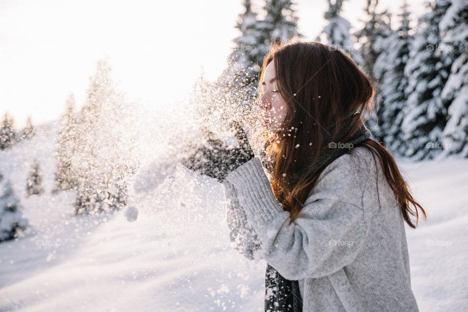 Woman playing with snow, while being in the mountains surrounded by a snowy landscape.