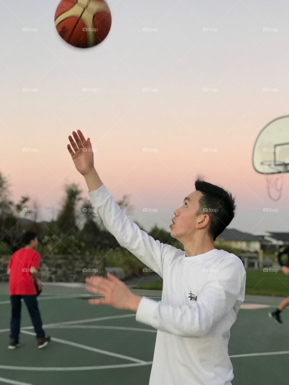  Attempting to catch the basketball coming from the distance with a beautiful multicoloured clouds from the sunset in progress in the background.