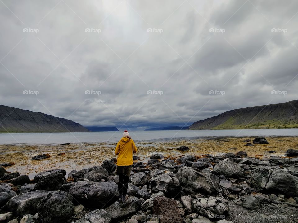 Morning walk of woman in yellow jacket on an empty beach during a cloudy day