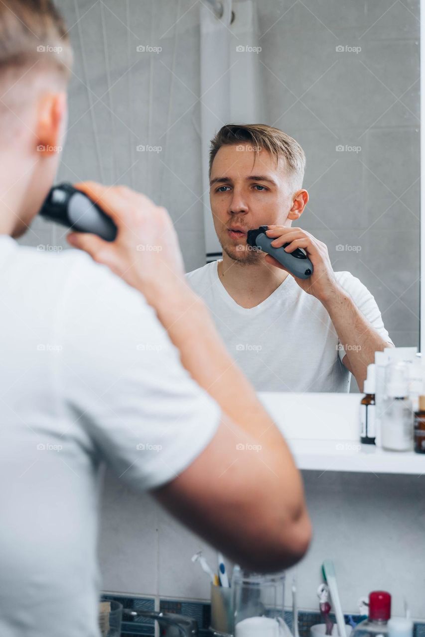 Man shaving his beard in bathroom using electric shaver 