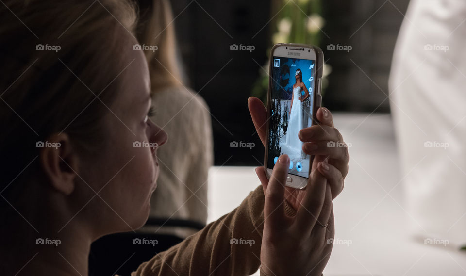 Woman taking picture with her cellular phone at a fashion show at a wedding fair.