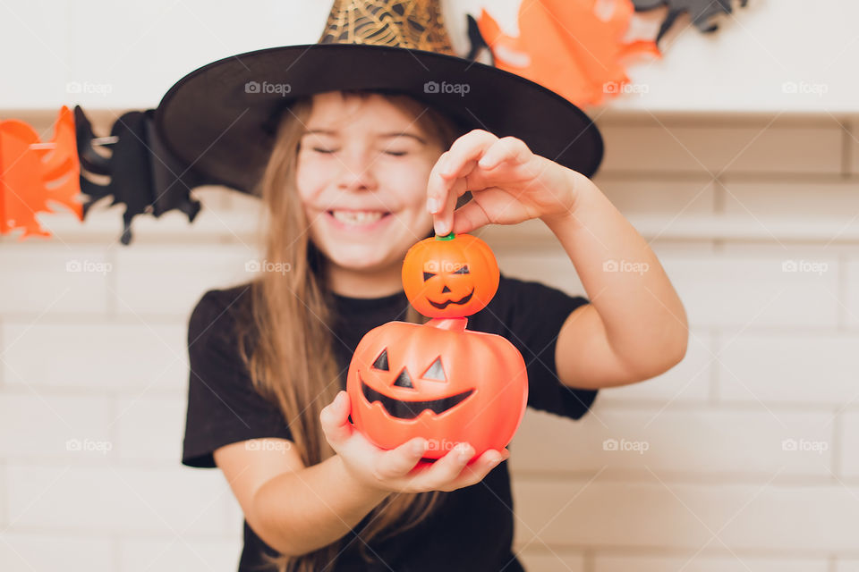 Little girl dressed as a witch for halloween holding a pumpkin with a face on the background decor