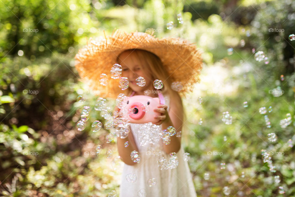 Happy little Caucasian girl with blonde hair wearing straw hat and having fun outdoor at summer 