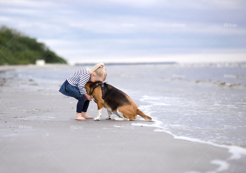 Little girl bare foot hugging dog at the sea