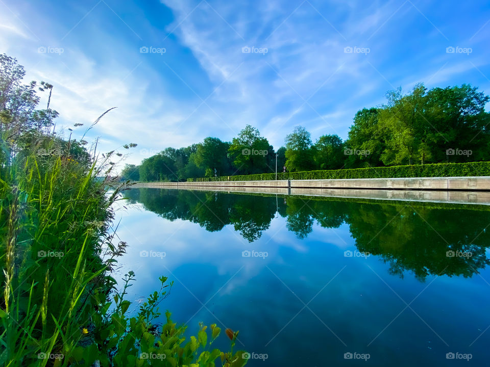 Clear blue sky reflected in the water between the lush green grass and trees