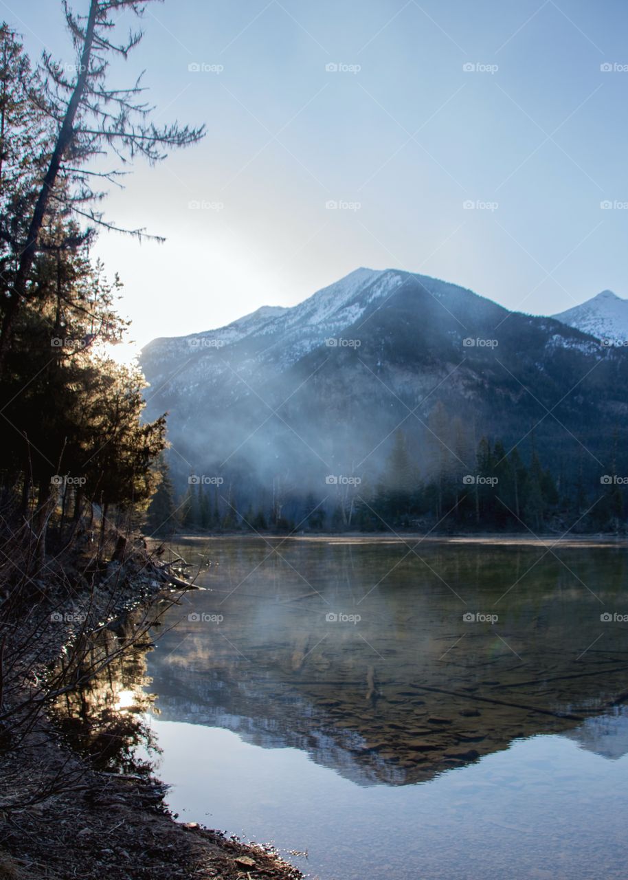 Reflection of snowy mountains on a fog covered lake at sunrise. 