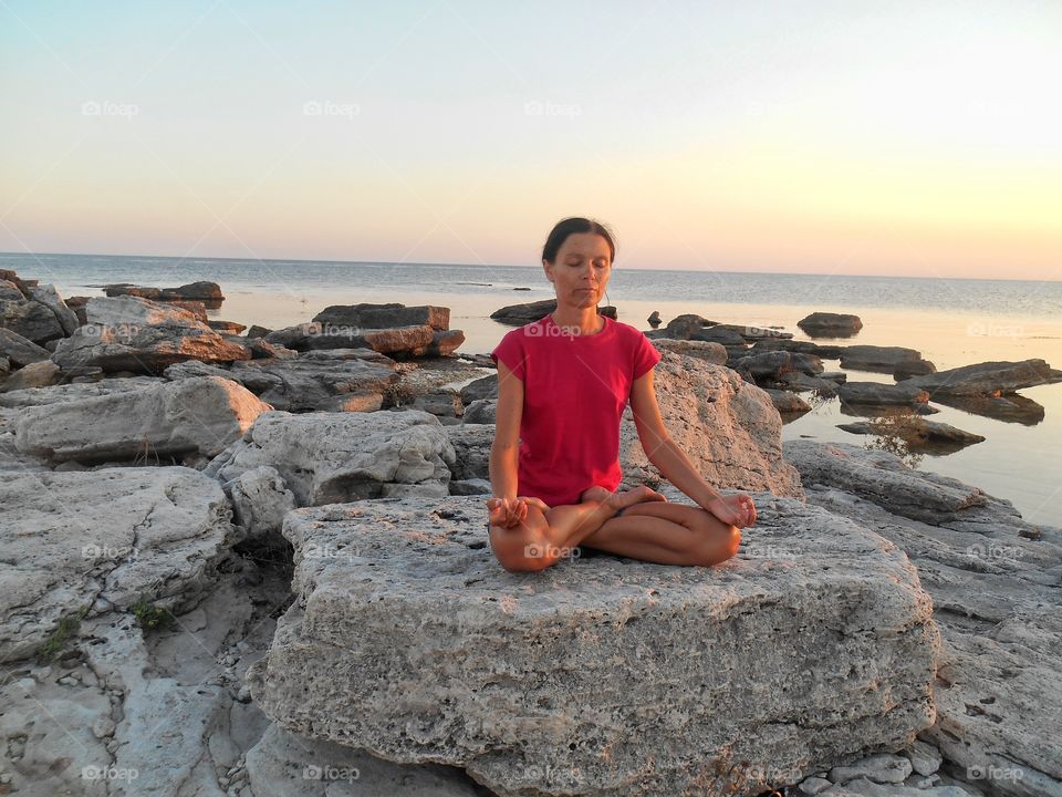 girl training yoga meditation on a sunset sea stone rock summer time