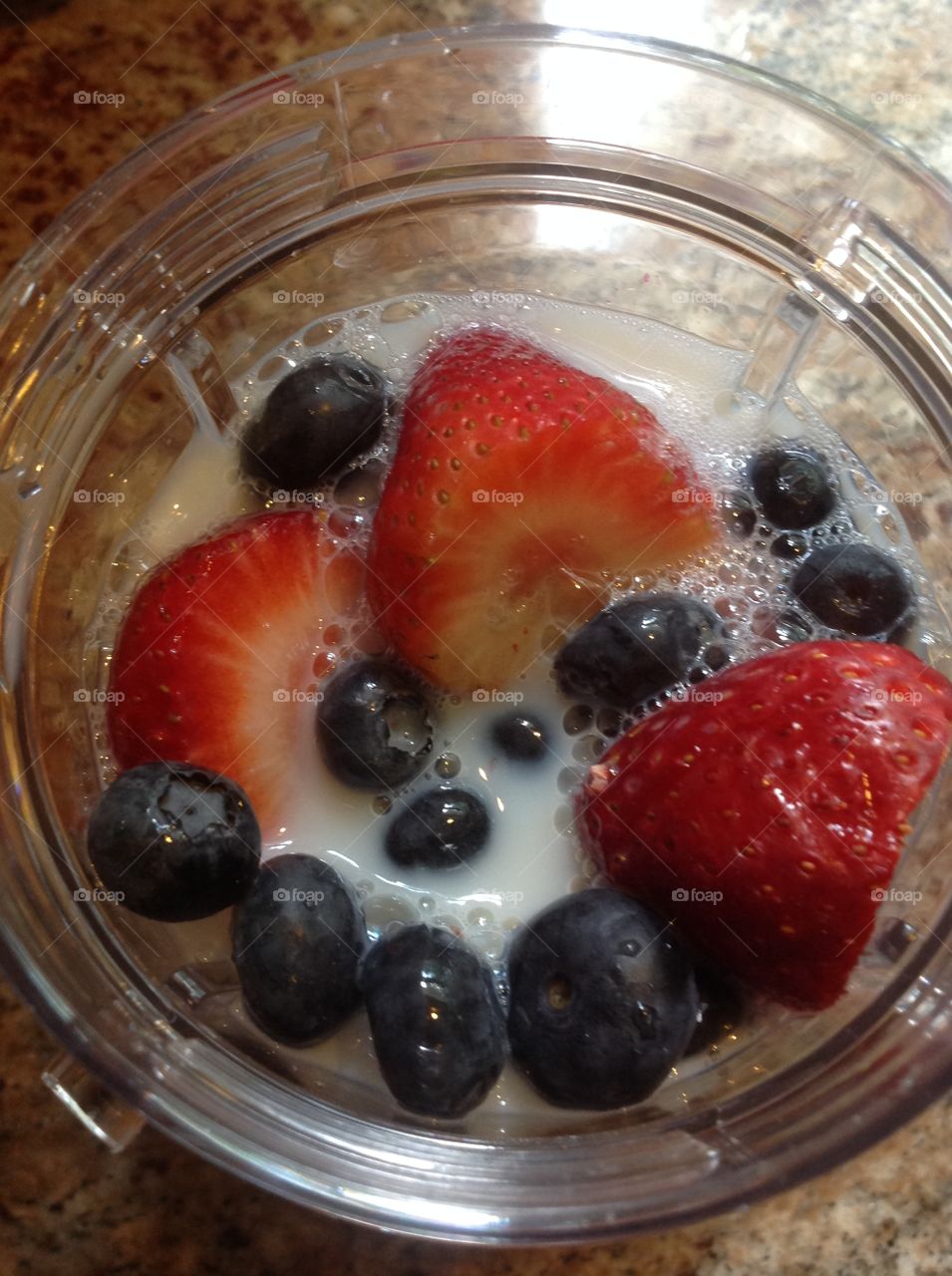 Strawberries and blueberries and milk getting ready to make a smoothie.