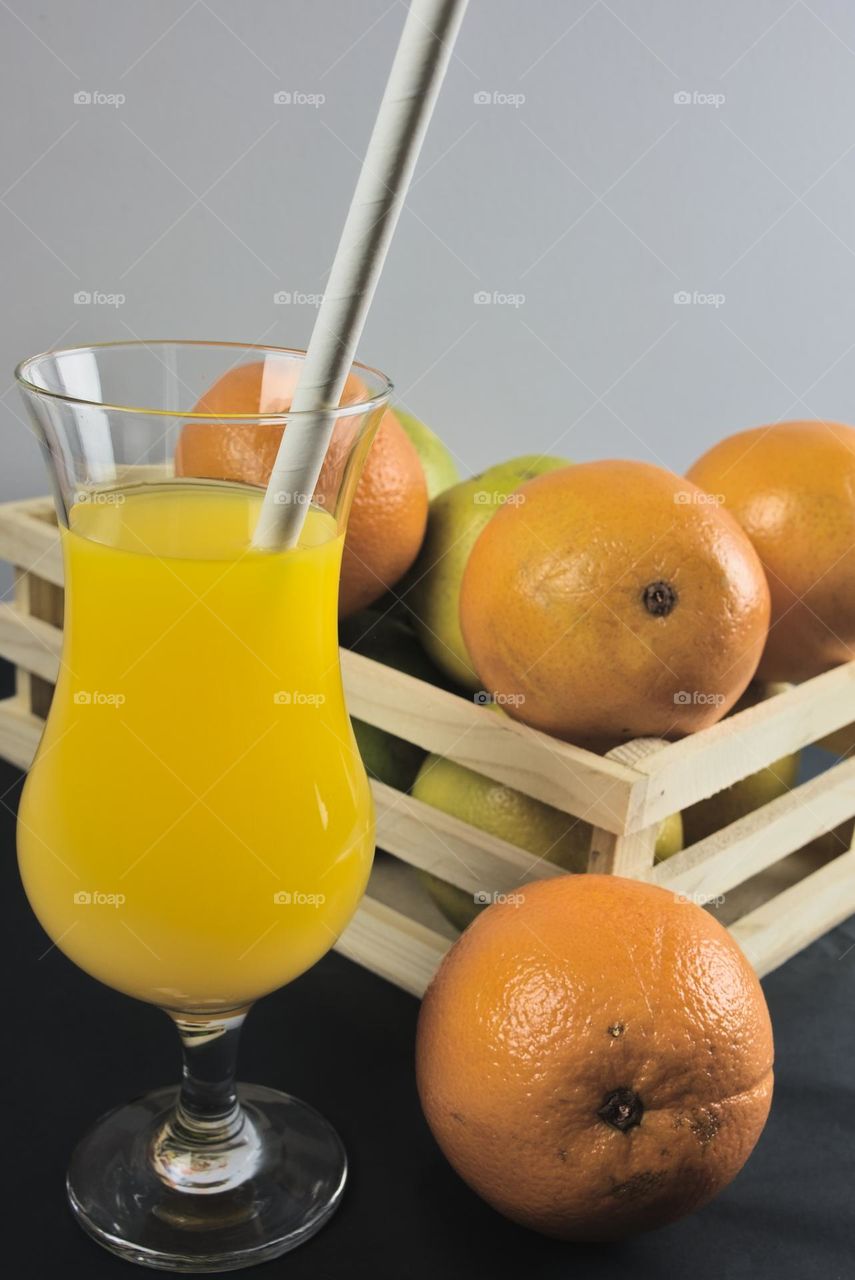 Oranges and glass tumbler with orange juice on black background