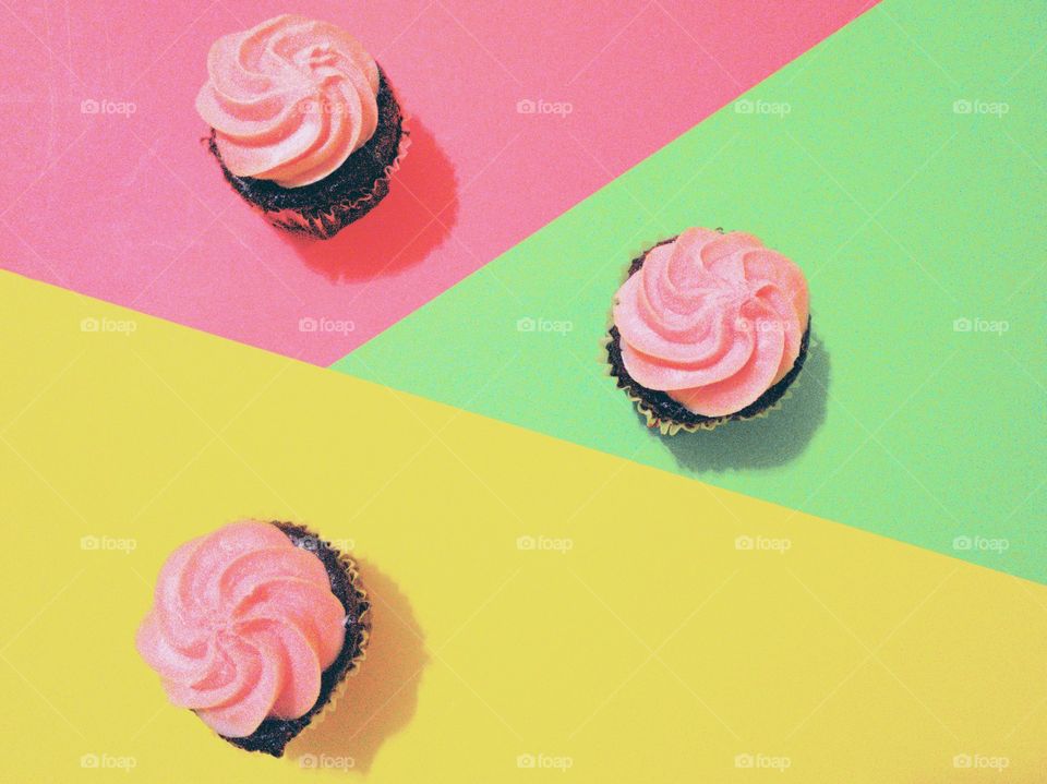 Three pink frosting chocolate cupcakes on a geometric triangle pink,  green and yellow surface