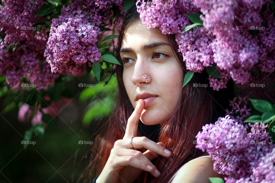 Nose piercing jewellery on a beautiful young woman in lilac flowers