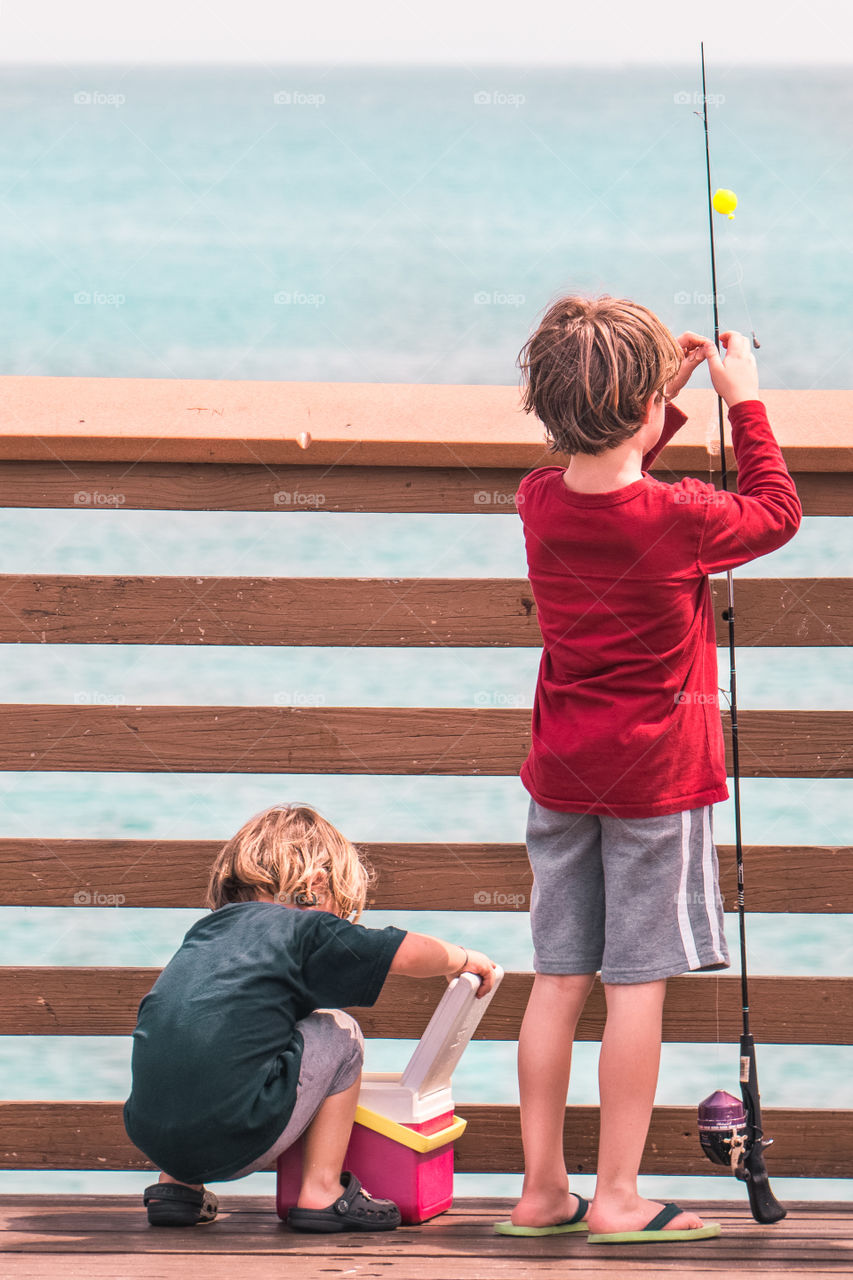 Two little boys fishing on the pier by the ocean beach