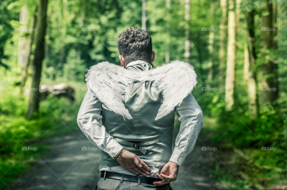 a man with wings of an angel goes through the forest