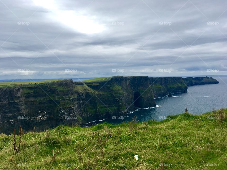 A beautiful photo of the Cliffs of Moher in Ireland with green grass and a cloudy sky 