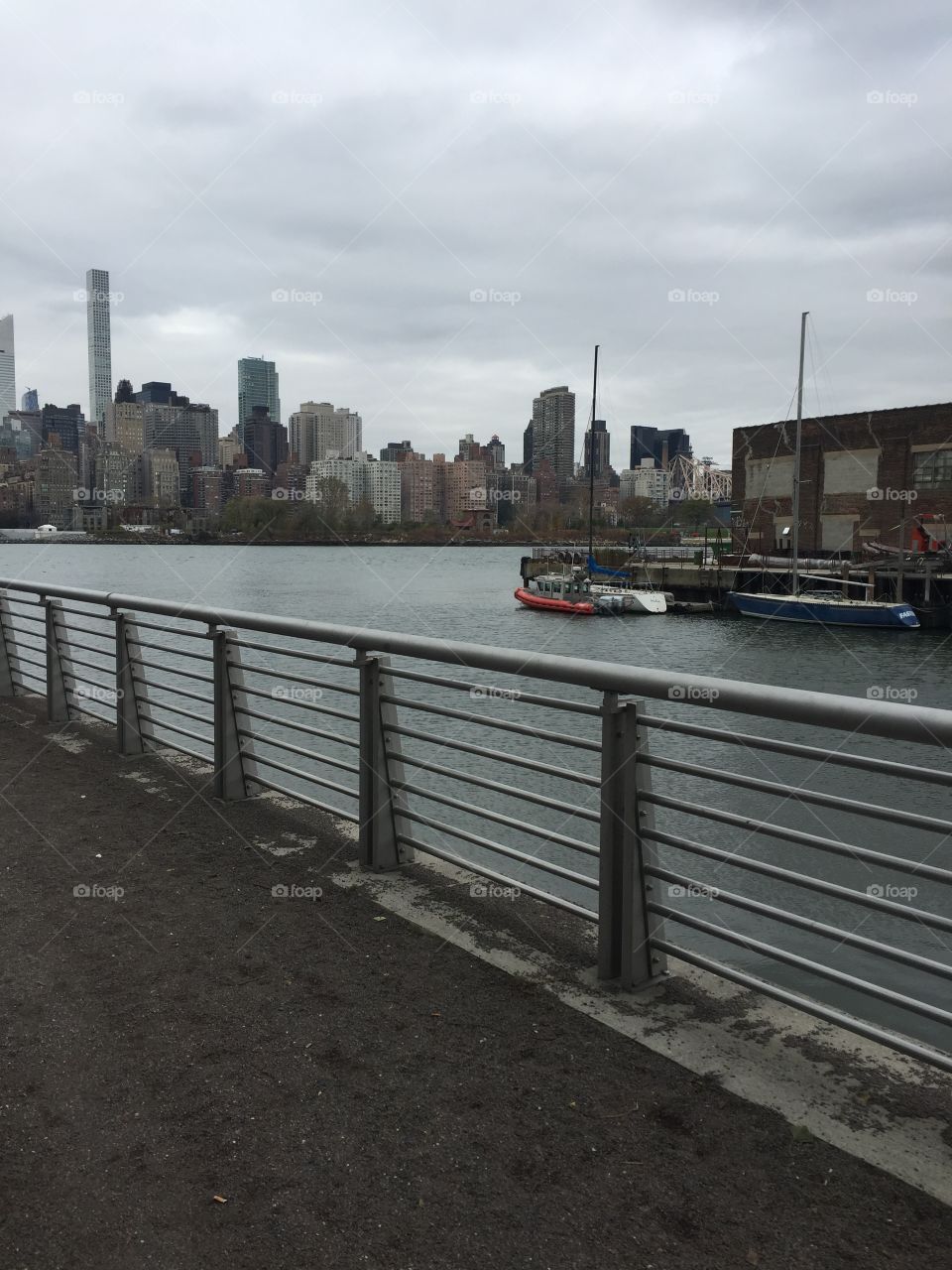 Photo of a city view taken from the boarding docks. You can see New York cities buildings and skyscrapers . Also shown is the river and finally a boat and the trail from where the photographer was standing.